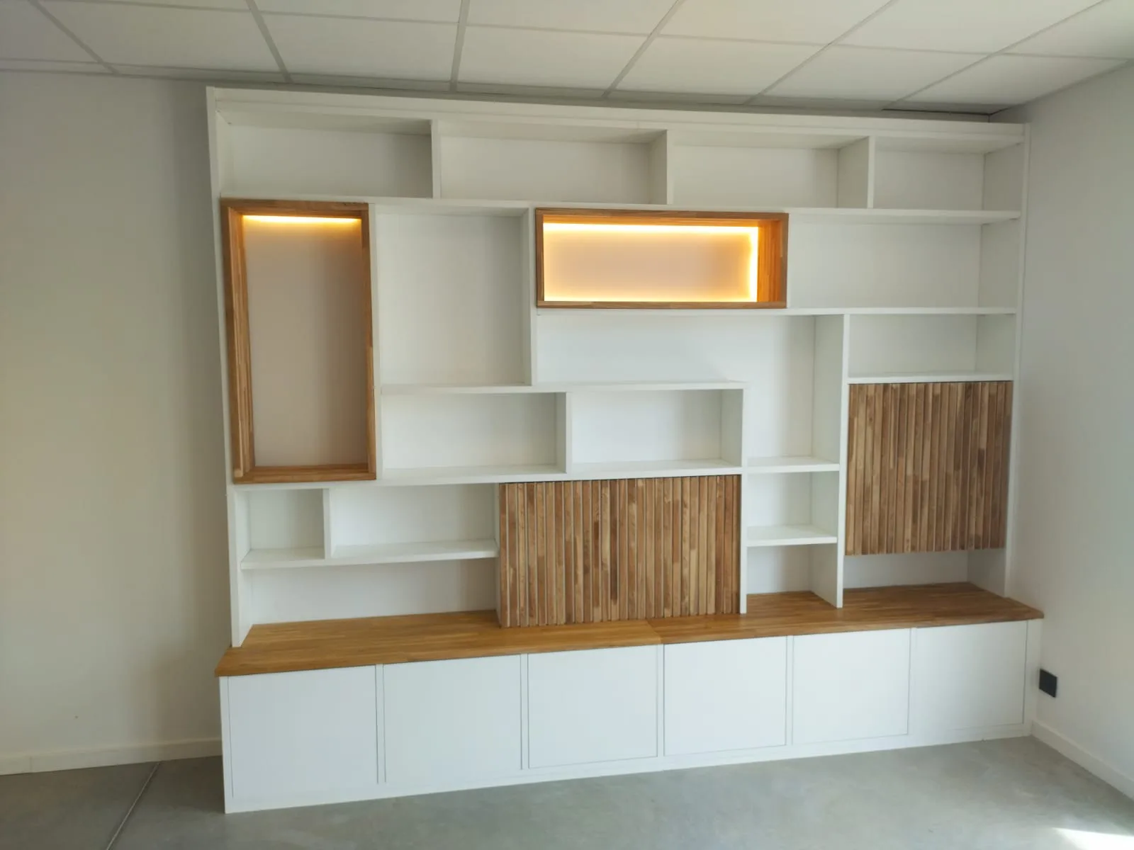 Bibliothèque blanche à niches chêne rétroéclairées, posée sur un plateau bois toute largeur