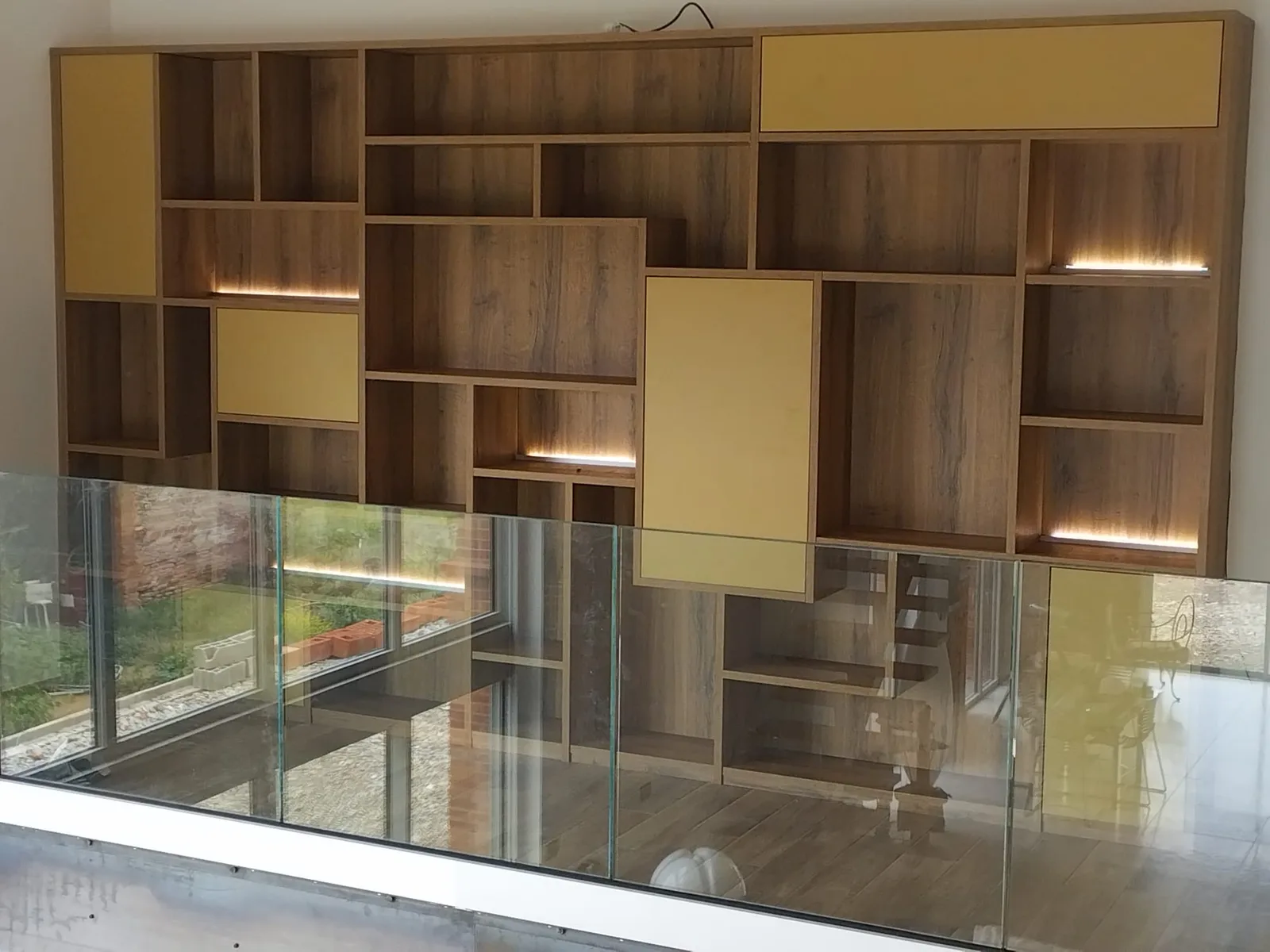 Bibliothèque toute hauteur en bois et jaune, montant jusqu'à la mezzanine, niches éclairées
